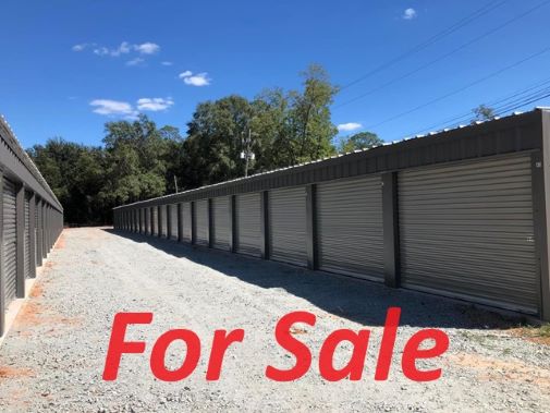 Image of storage unit with gravel driveway and "for sale" in red type